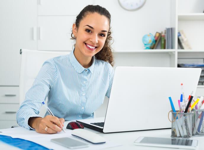 A smiling female administrative assistant in an office after completing her administrative assistant diploma program